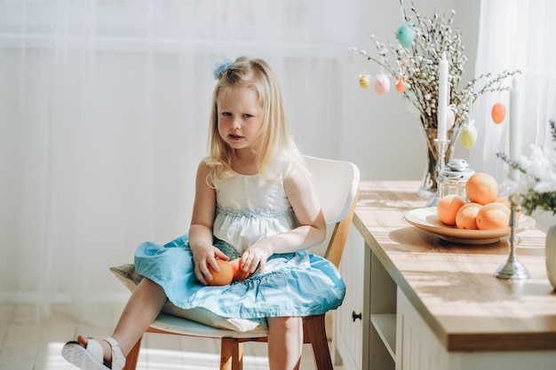 부활절 휴일 준비 작은 소녀는 휴일을 기대하며 손에 과일을 들고 방에서 의자에 앉아 있습니다.