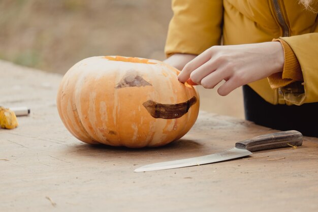 写真 ハロウィーンの準備：カボチャを切る女の子。閉じる。休日の装飾の概念。女性はジャック・オー・ランタンを準備します。デコレーションパーティー。リトルヘルパー。