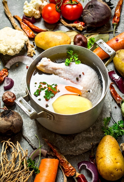 Preparation of fragrant chicken soup with fresh vegetables on stone table.