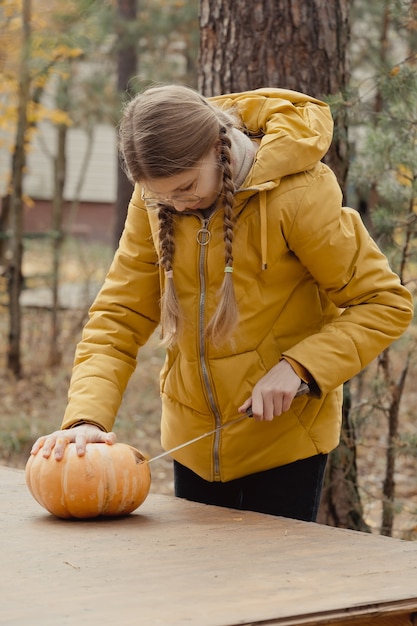 Preparation for Halloween: girl cutting pumpkin. Closeup. Holiday decoration concept. Woman prepares jack-o-lantern. Decoration party. Little helper.