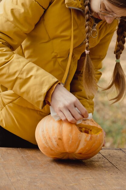 ハロウィーンの準備：女の子はカボチャの種を抽出します。閉じる。休日の装飾の概念。女性はジャック・オー・ランタンを準備します。デコレーションパーティー。リトルヘルパー。