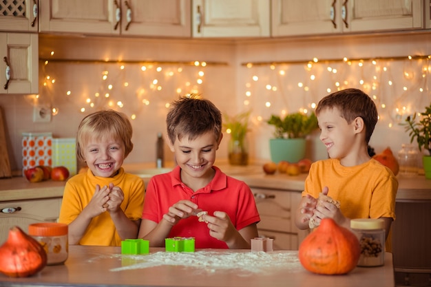 ホリデーハロウィーンの準備。 3人の陽気な子供がキッチンでクッキーを作る