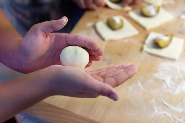 Приготовление домашних фруктовых пельмени с сливами Чешская специальность сладкой хорошей еды Тесто на кухонном деревянном столе с руками