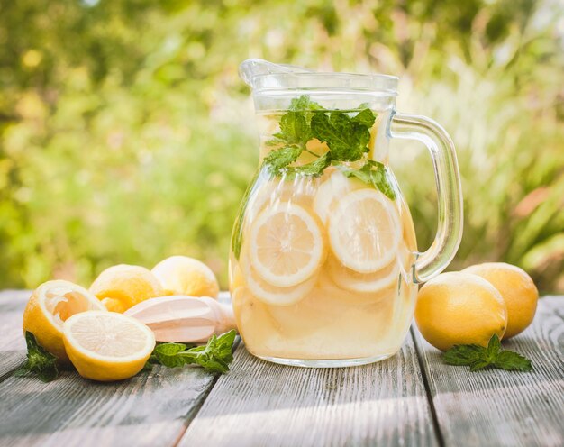 レモネードドリンクの準備。水差しのレモネードと屋外のテーブルにミントとレモン
