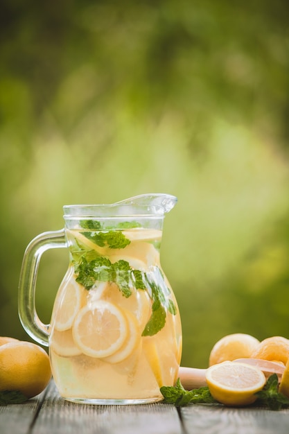 Preparation of the lemonade drink. Lemonade in the jug and lemons with mint on the table outdoor