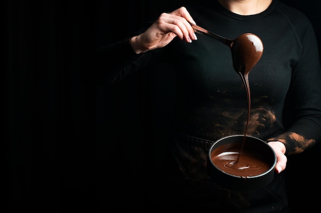 黒い背景にショコラティエの手で溶かしたチョコレートの準備キッチン泡立て器