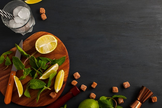 Preparation of Mojito cocktail. Bar utensils and ingredients mint, lime, ice and cane sugar. Top view with copy space