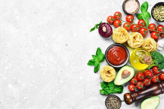 Preparation of pasta Dry pasta and ingredients tomatoes basil pepper and rosemary on a gray stone background Dry pasta Top view Free space for text