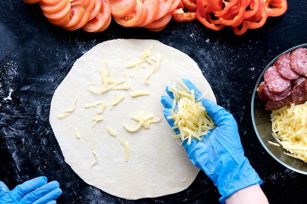 Preparation pizza in restaurant in silicone gloves on black table 