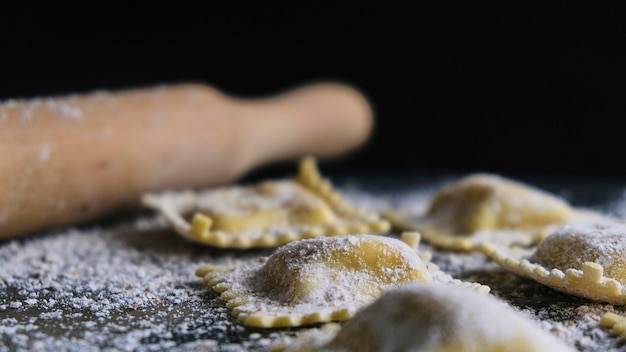 Preparation of Ravioli. Fresh pasta on black background. Darkfood with flour and a rolling pin