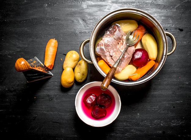 Preparation of soup from fresh vegetables. On a black wooden background.