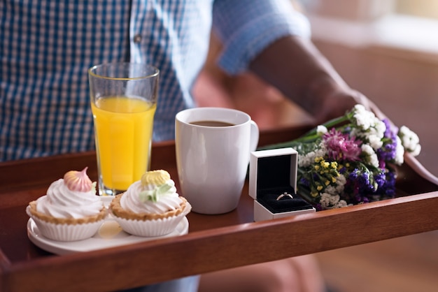 Foto tempi di preparazione. primo piano di un vassoio con colazione e fede nuziale detenuta da giovane africano che si prepara per fare una proposta alla sua ragazza.