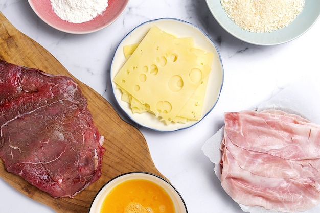 Preparation of traditional homemade milanesa veal escalope with flour, egg, breadcrumbs, cheese and ham