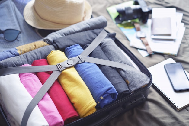 Prepare accessories for journey and travel to long weekend trip, packing clothes in suitcase bag on bed.