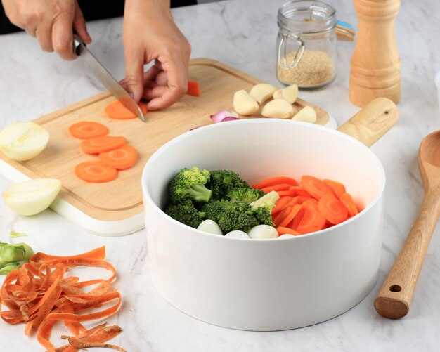 Prepare Cooking, Slicing Carrots Above Wooden Chopping Board. Female Hand Cooking Vegetables in the Kitchen