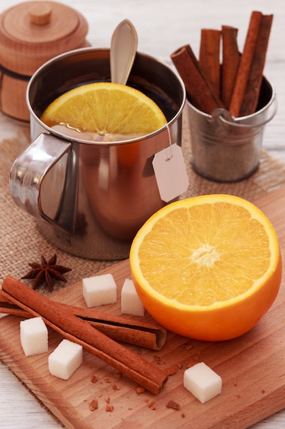 Preparing of black tea in metallic cup with orange fruit and cinnamon sticks