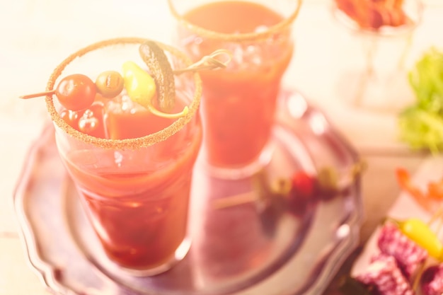 Preparing bloody mary cocktail garnished with celery sticks, olives, and bacon strips.