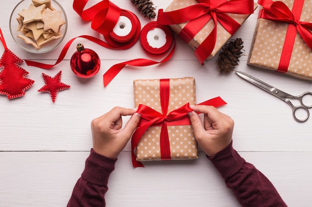 Preparing for Christmas holidays. Female hands wrapping gift box, top view