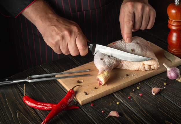 Подготовка к приготовлению куриных ножек на кухне Шеф-повар режет сырую куриную ножку ножом на разделочной доске Курица на гриле