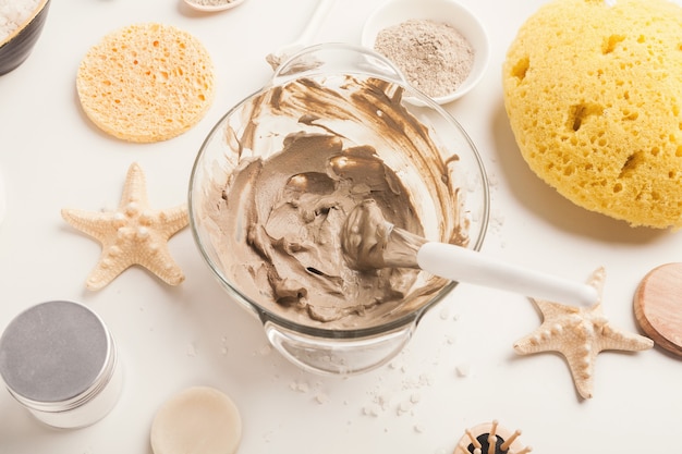 Preparing cosmetic mud mask in glass bowl on white background. Closeup texture of facial clay emulsion. Natural cosmetics for home or salon spa treatment