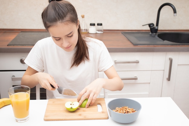 美味しくてヘルシーな朝食を用意しています。キッチンで若い女性が新鮮な果物でミューズリーを準備しています。