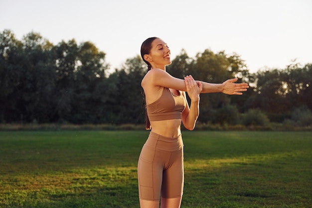 Preparing for the fitness session Young woman in yoga clothes is outdoors on the field