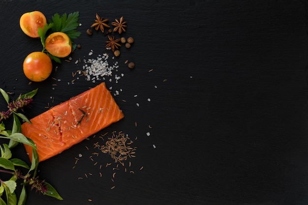 Foto preparazione di frutti di mare freschi in cucina con filetto di salmone gourmet circondato da erbe fresche e spezie su sfondo di pietra nera