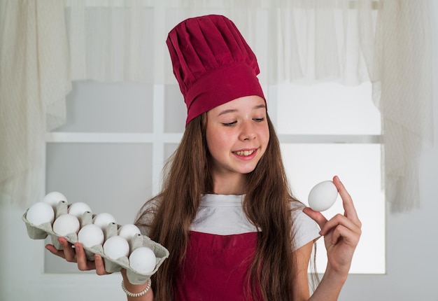 Preparing from eggs happy child wear cook uniform chef girl in hat and apron kid cooking food in kitchen choosing a career little helper with eggs culinary and cuisine happy childhood