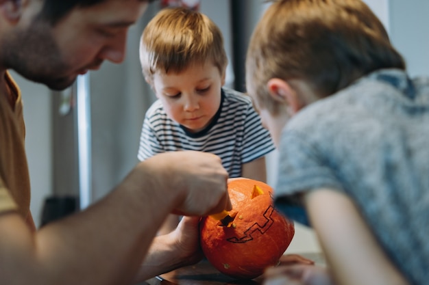 ハロウィーンのお祝いの準備。白人男性は、カボチャに目を彫って伝統的なジャックランタンを作るかわいい息子たちと一緒にいます。セレクティブフォーカスの画像。