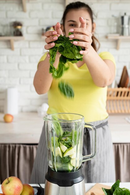 健康的な食品の準備健康的な食事とダイエット家庭の台所で緑のスムージーを作る若いブルネットの女性