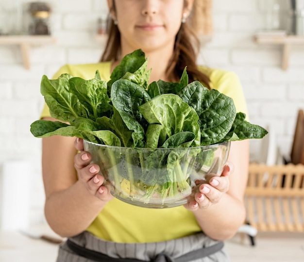 Preparing healthy foods Healthy eating and dieting Young caucasian brunette woman holding a bowl of fresh spinach in the kitchen