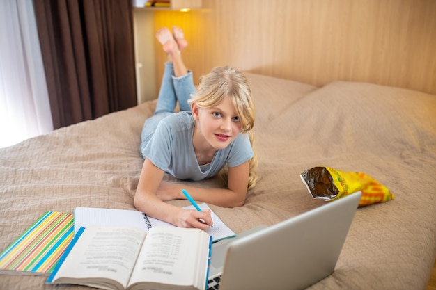 Foto preparare i compiti. una ragazza bionda sdraiata sul letto e facendo le sue lezioni