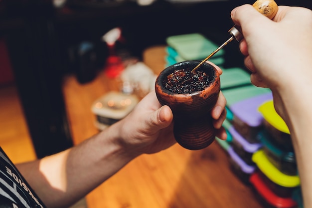 Preparing hookah for smoking, filling clay bowl with tobacco, male hands visible.