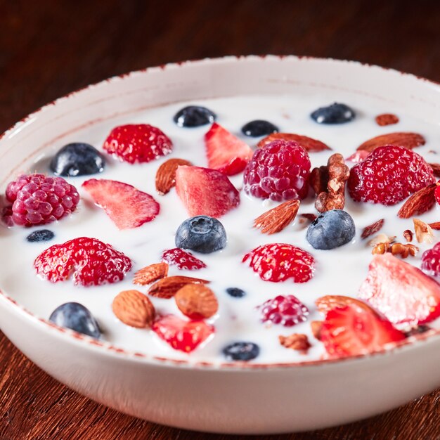 Preparazione della colazione naturale con ingredienti biologici freschi - bacche, muesli, noci, miele e versando il latte in una ciotola bianca su un tavolo di legno. mangiare vegetariano detox