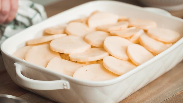 Preparing scalloped potatoes in a white ceramic baking dish.