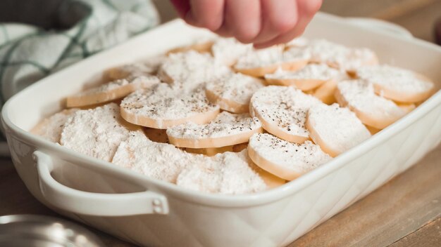 Preparing scalloped potatoes in a white ceramic baking dish.