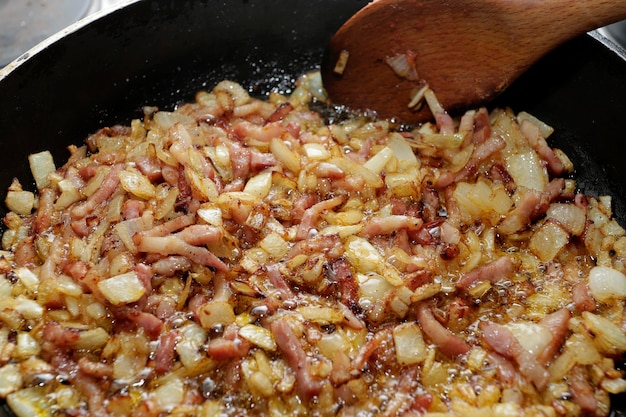 preparing sofrito with onion and bacon in a frying pan