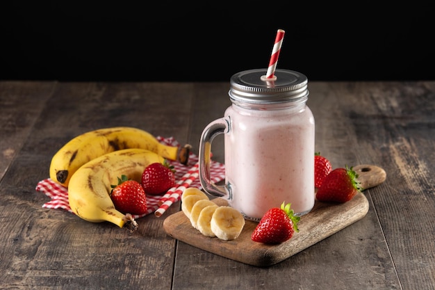 Preparing strawberry and banana smoothie in jar on wooden table