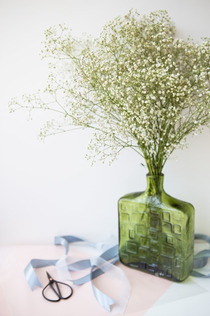 写真 結婚式の花束を準備すると、白いカスミソウの花の花束がリボンとはさみと一緒に緑の花瓶に立っています。