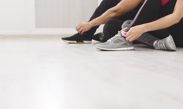 Preparing for training. Unrecognizable couple tying shoelaces sitting on the floor in studio, panorama, copy space