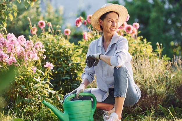 Preparing for watering the flowers Young cheerful woman is in the garden at daytime