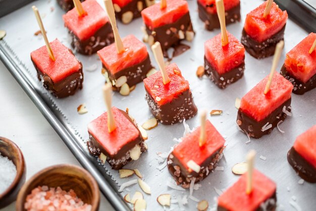 Preparing watermelon appetizers dipped in chocolate and sprinked with sea salt and almonds.