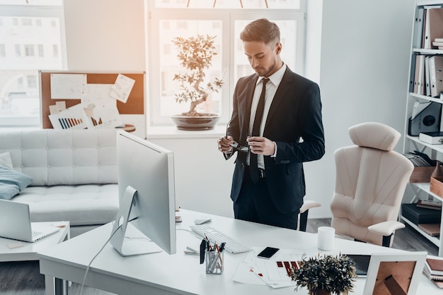 Preparing to work hard. Good looking young man in full suit holding eyeglasses 