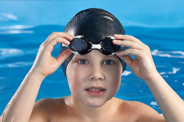 사진 수영 모자와 고글을 쓰고 수영장에서 수영하는 법을 배우는 취학 전 소년