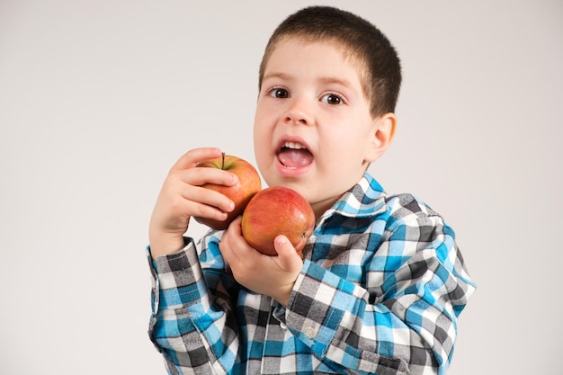 格子縞のシャツを着た就学前の男の子は赤いリンゴを持っています