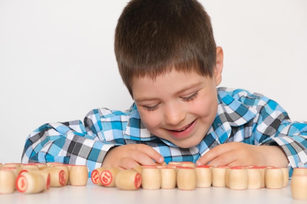 A preschool boy plays lotto folds barrels with numbers on the table