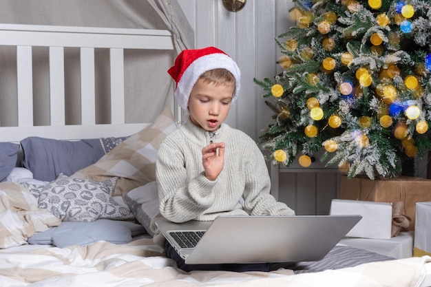 A preschool boy in a santa hat communicates via video link explaining which gift he wants to receive in a room