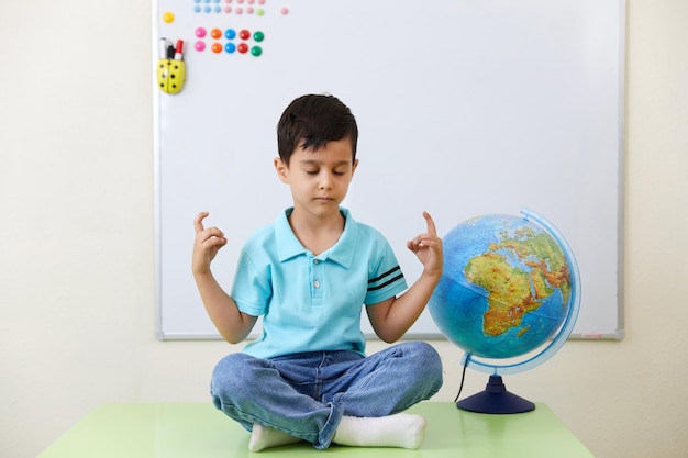 Preschool boy sitting wih book in classroom with globe