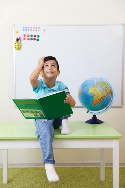 Preschool boy sitting wih book in classroom with globe