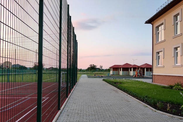 Cantiere della scuola materna con campo da basket circondato da alta recinzione protettiva